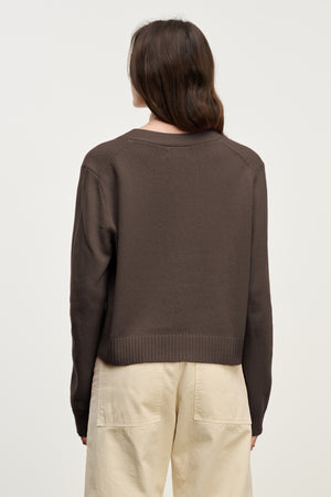 A person with long brown hair is shown from behind, wearing the ETNA CARDIGAN by Velvet by Graham & Spencer—a dark brown wool blend—over light-colored pants against a plain background.