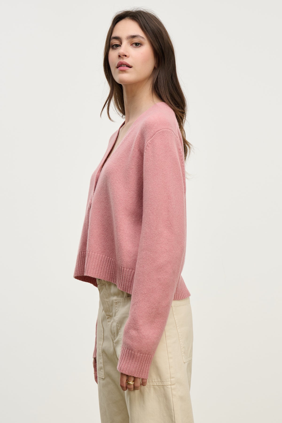 A person wearing the ETNA CARDIGAN by Velvet by Graham & Spencer, featuring a loose fit and V-neckline, pairs it with light beige pants against a plain background—a perfect layering piece for any look.-40227054780609