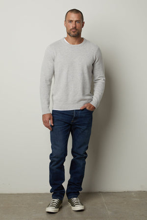 A stylish man wearing a Velvet by Graham & Spencer DASHELL CREW NECK SWEATER posing in front of a white wall.