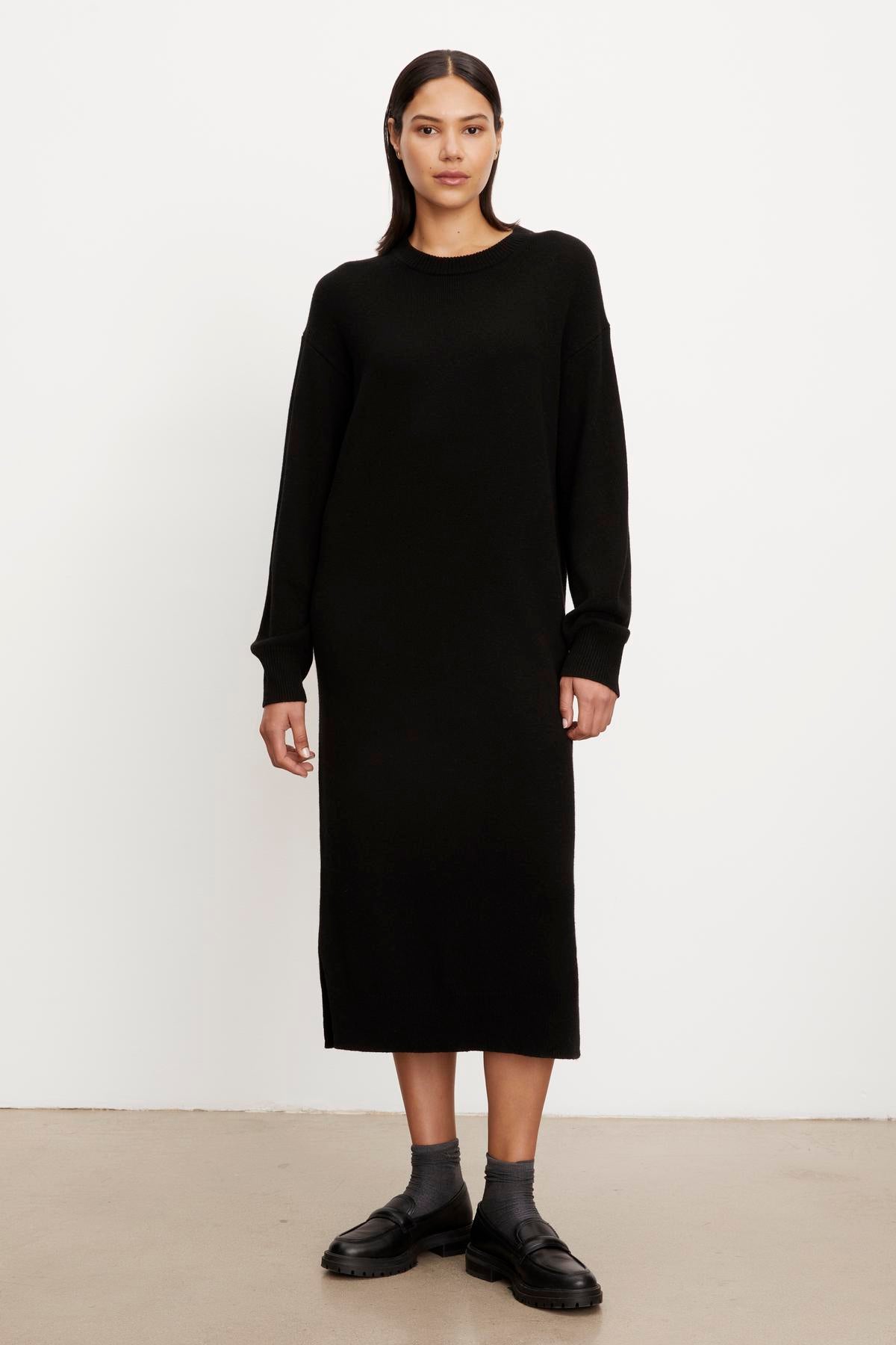   A woman in a Kaden sweater dress by Velvet by Graham & Spencer with a crew neckline and black loafers standing against a plain white background. 
