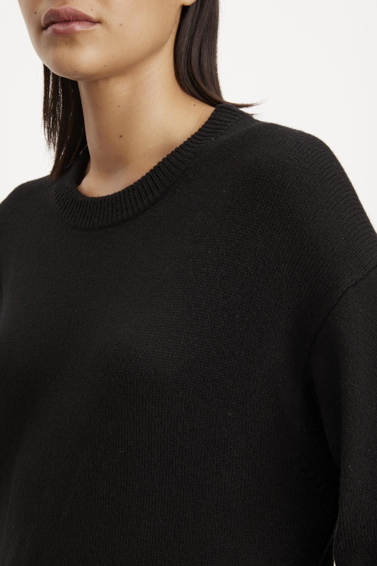   Close-up of a woman wearing a black ribbed Kaden sweater dress by Velvet by Graham & Spencer, focusing on the crew neckline and upper chest area. 