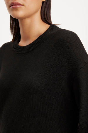 Close-up of a woman wearing a black ribbed Kaden sweater dress by Velvet by Graham & Spencer, focusing on the crew neckline and upper chest area.