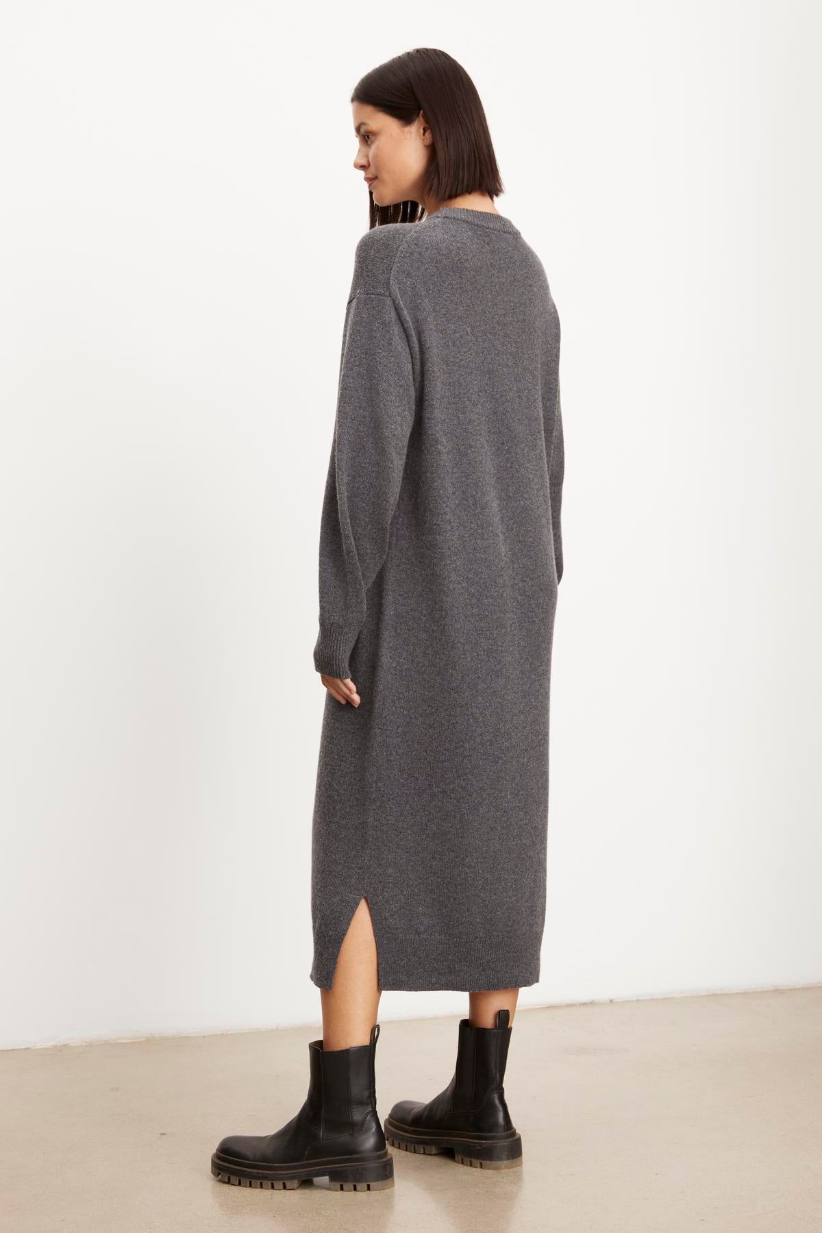   Woman in a long grey cardigan and black boots, standing sideways against a white background, wearing Velvet by Graham & Spencer's KADEN SWEATER DRESS with a side split hem. 
