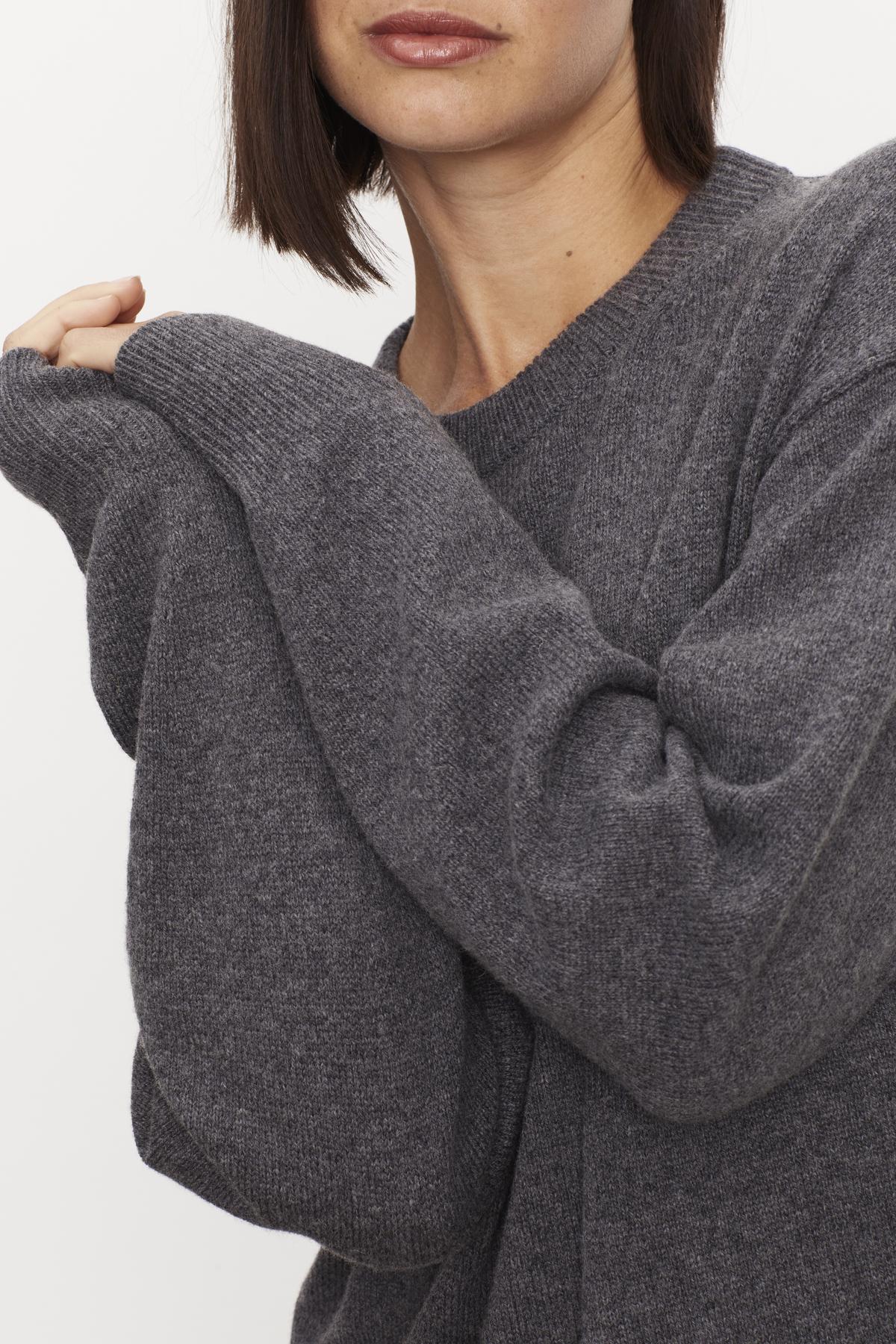   Woman in a Gray Kaden Sweater Dress by Velvet by Graham & Spencer with a crew neckline, partial face visible, holding her sleeve with one hand. Close-up emphasizes the dress's texture. 