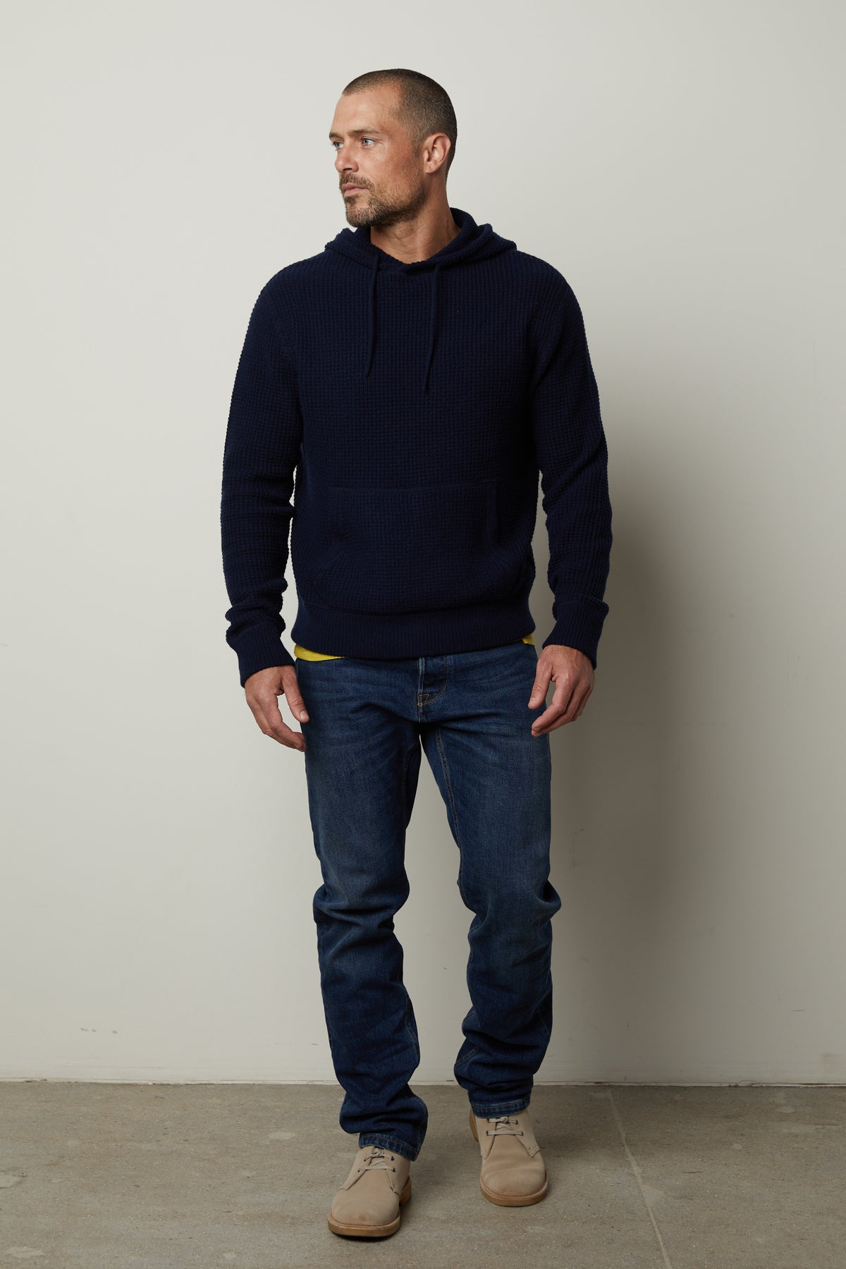   A man wearing jeans and a Velvet by Graham & Spencer SHANE SWEATER HOODIE standing in front of a wall. 