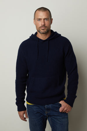 A man wearing a Velvet by Graham & Spencer SHANE SWEATER HOODIE and jeans.