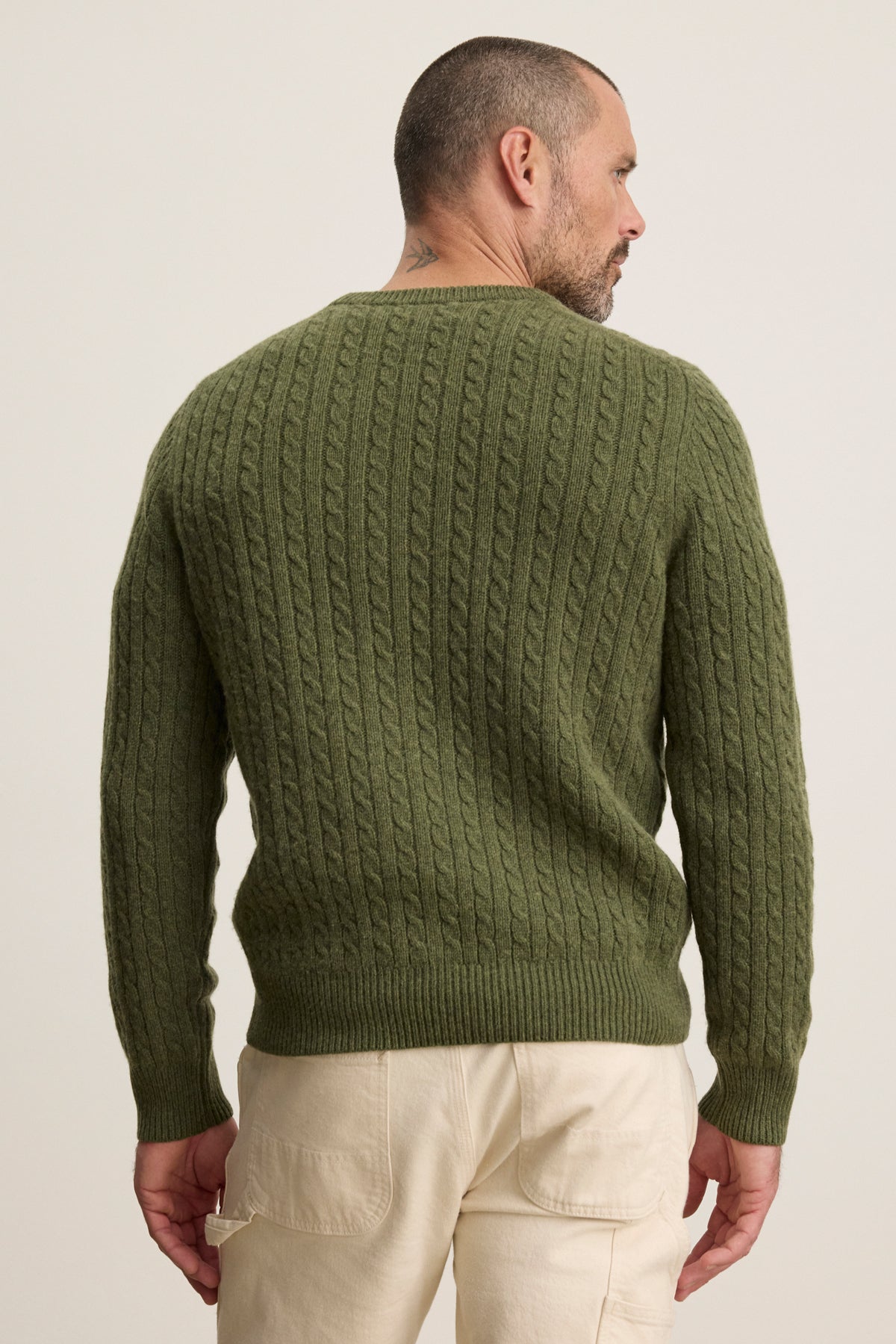   A man faces away from the camera, wearing the ALONZO SWEATER by Velvet by Graham & Spencer in olive green and light beige pants. 