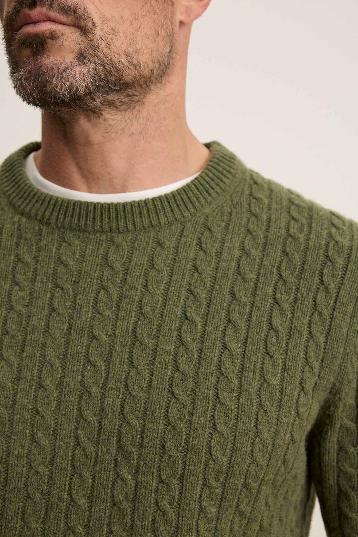 Close-up of a man wearing the ALONZO SWEATER by Velvet by Graham & Spencer, a green wool-blend cable-knit, layered over a white crew neck shirt, with part of his face and beard visible.-39934266671297