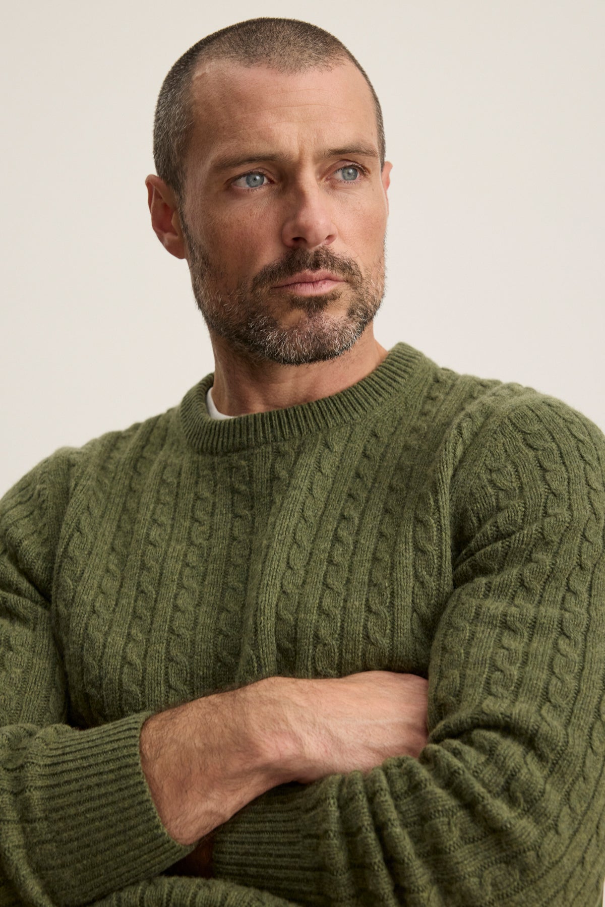 A man with short hair and a beard wears the green ALONZO SWEATER by Velvet by Graham & Spencer, standing with arms crossed and gazing slightly to the side.-39934266704065