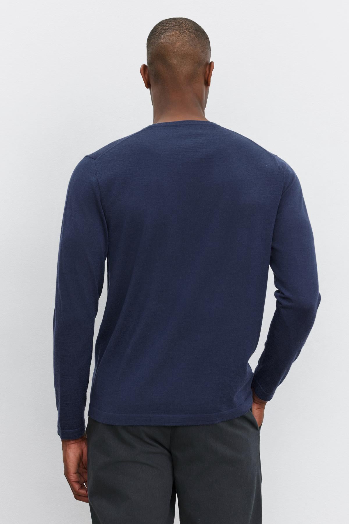 A man stands facing away from the camera wearing an ALVIN SWEATER by Velvet by Graham & Spencer and dark gray pants against a plain background.-37681887084737