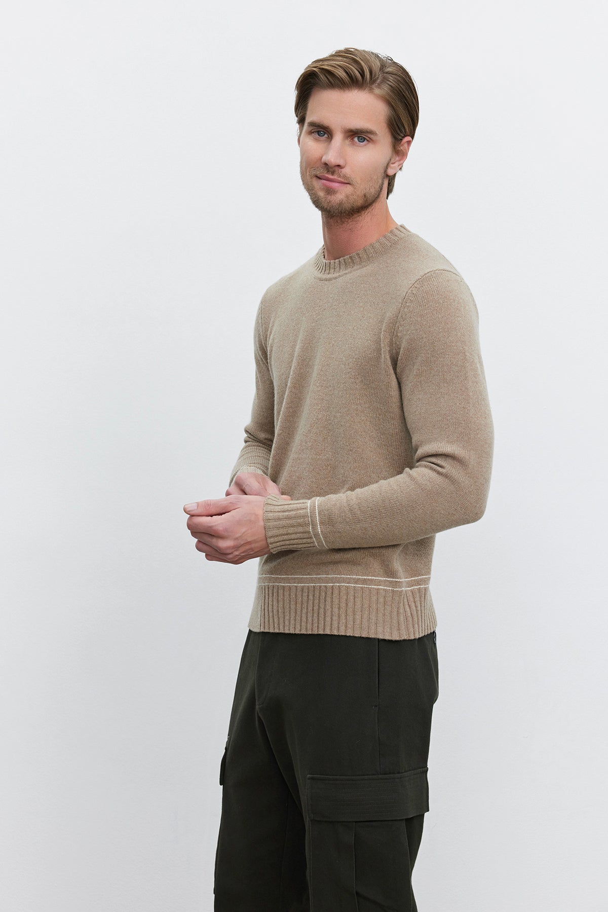   A man with light brown hair stands against a plain background wearing the ATTICUS SWEATER by Velvet by Graham & Spencer and dark green pants. 