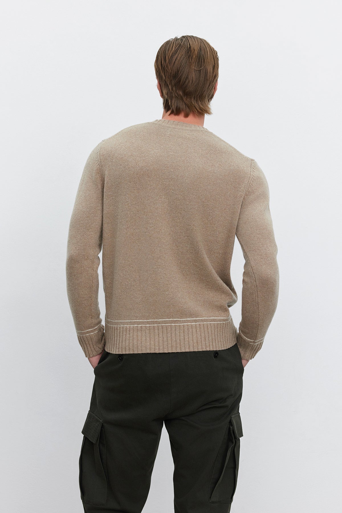   A person with brown hair is seen from the back, wearing the ATTICUS SWEATER by Velvet by Graham & Spencer in a beige wool blend and dark green cargo pants. 