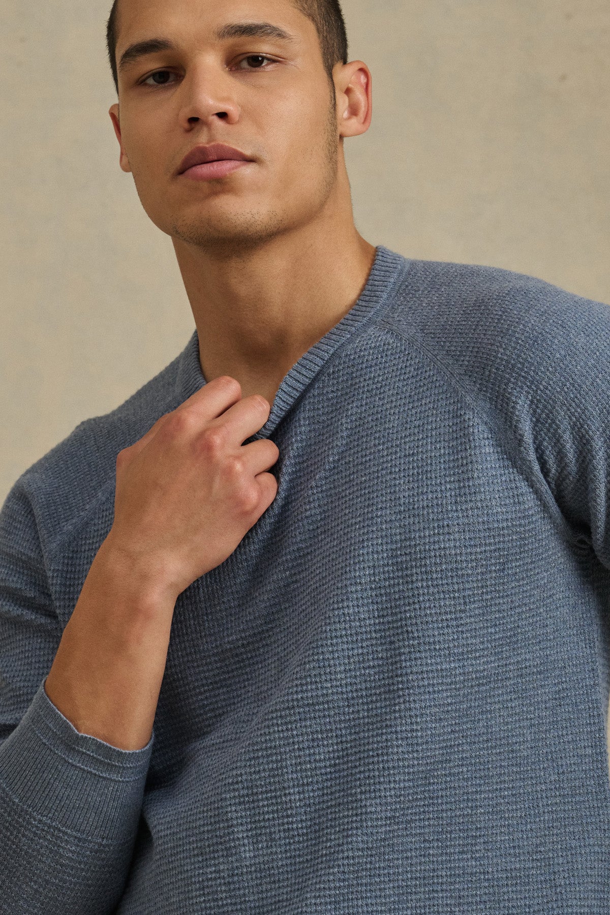 A person wearing the AUGIE SWEATER by Velvet by Graham & Spencer—a textured, long-sleeve blue cotton-cashmere crewneck—stands against a neutral background, holding the collar.