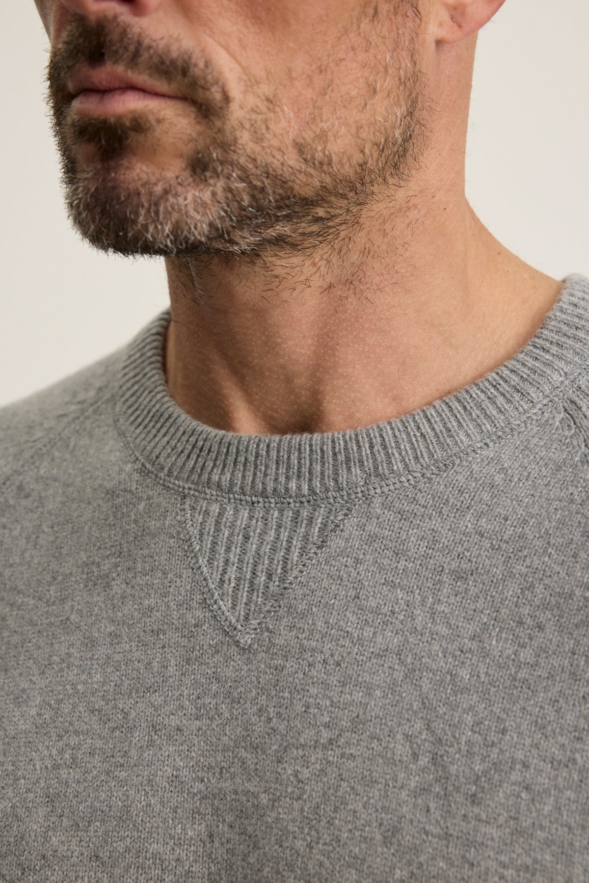 Close-up of a man's lower face, neck, and upper chest wearing the CORTEZ SWEATER by Velvet by Graham & Spencer, featuring a light grey knit with a ribbed collar.-40054234579137