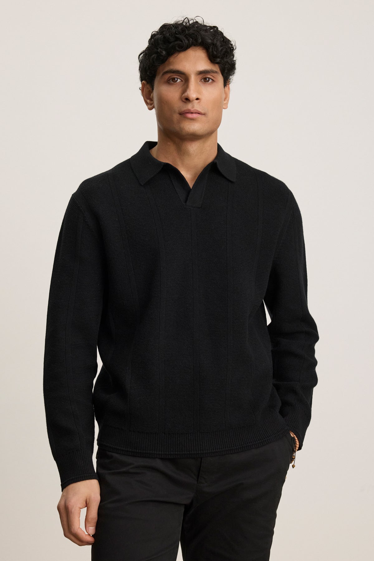 A person with short curly hair wears the REDDING SWEATER POLO by Velvet by Graham & Spencer and black pants, standing against a plain light background.-40054247817409