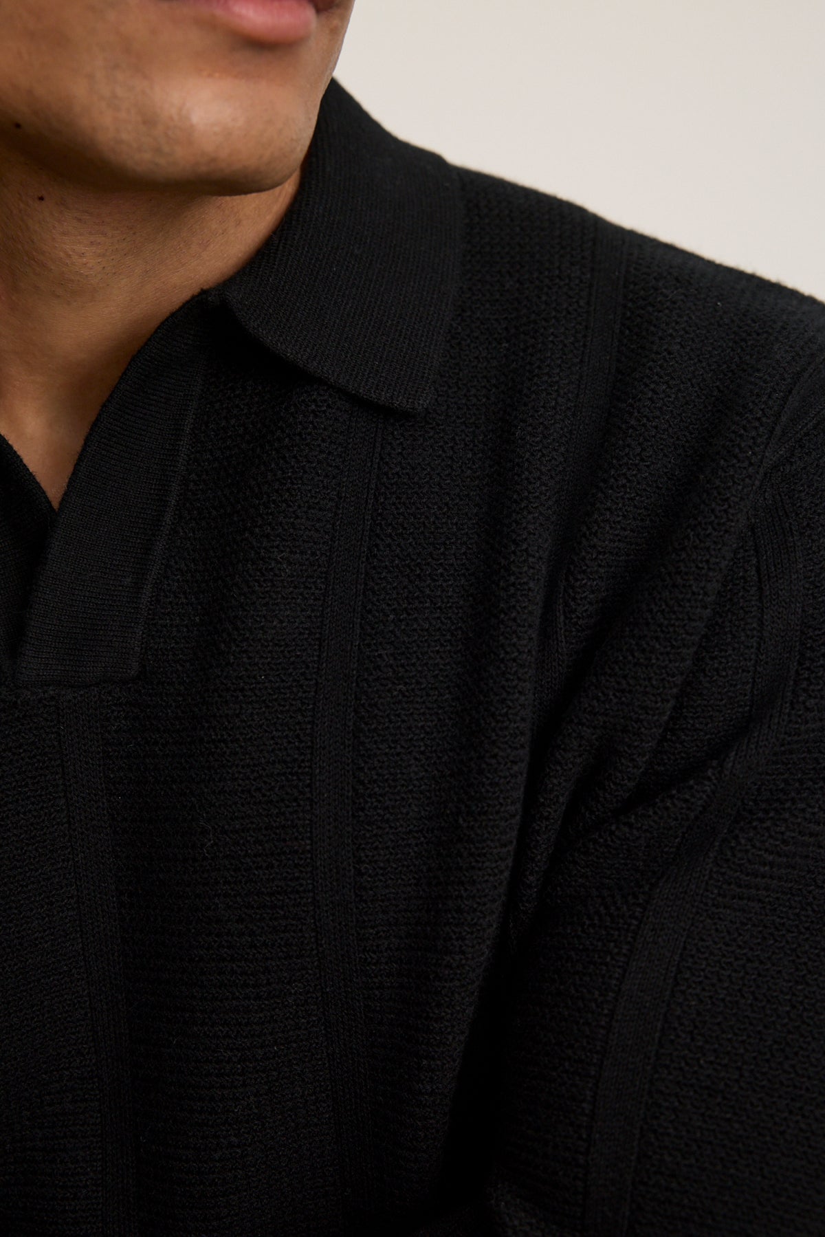 Close-up of a person wearing the REDDING SWEATER POLO by Velvet by Graham & Spencer—a textured black cotton-wool blend—showing part of their face, neck, and upper torso against a plain background. Perfect for versatile layering.-40054247948481