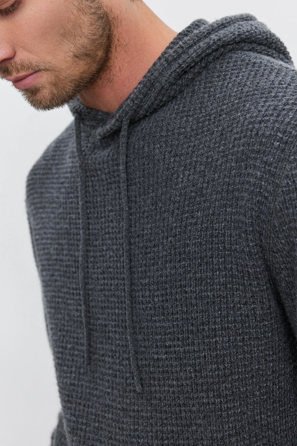 A man wearing a SHANE SWEATER HOODIE by Velvet by Graham & Spencer, in textured gray with visible drawstrings, photographed from the shoulders up, exuding warmth and comfort.-37893929894081