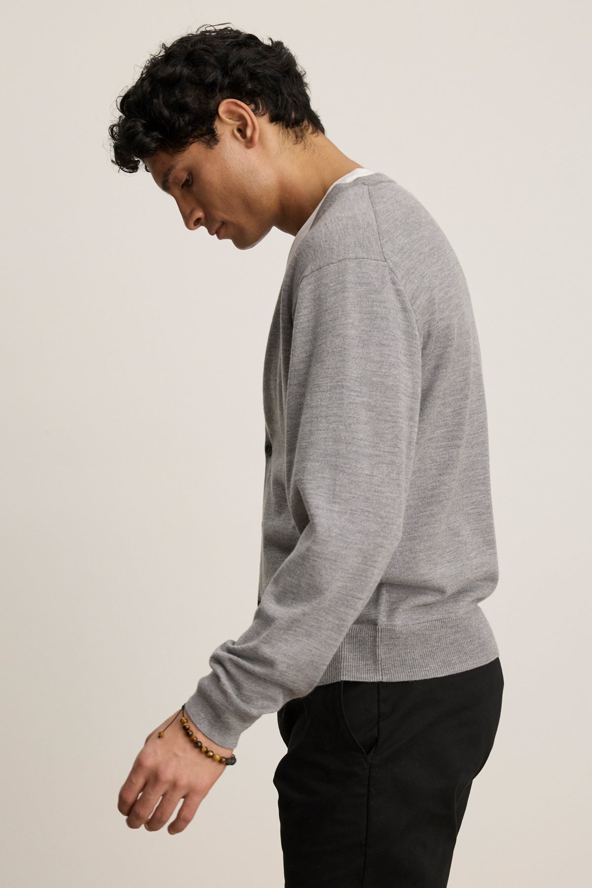 A person with short dark hair, wearing the SILVIO CARDIGAN by Velvet by Graham & Spencer and black pants, stands sideways against a plain light background.-39841095712961