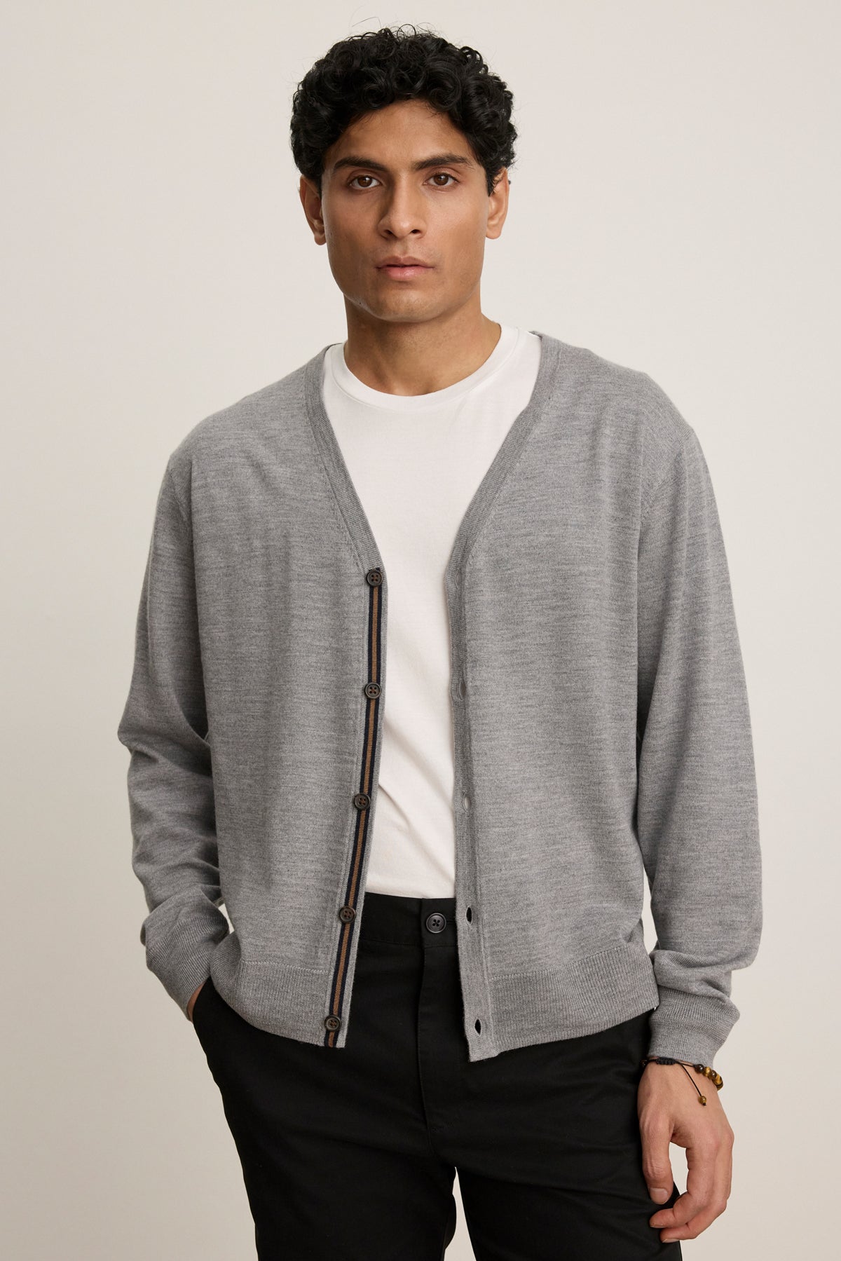 A man stands facing forward with a neutral expression, wearing the SILVIO CARDIGAN by Velvet by Graham & Spencer in light gray over a white t-shirt and black pants.-39841095745729
