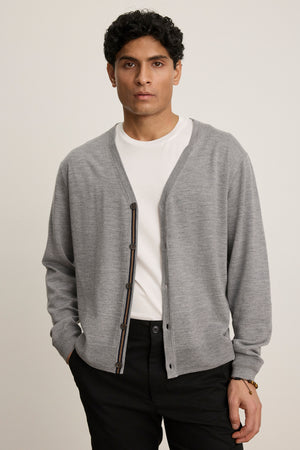 A man stands facing forward with a neutral expression, wearing the SILVIO CARDIGAN by Velvet by Graham & Spencer in light gray over a white t-shirt and black pants.