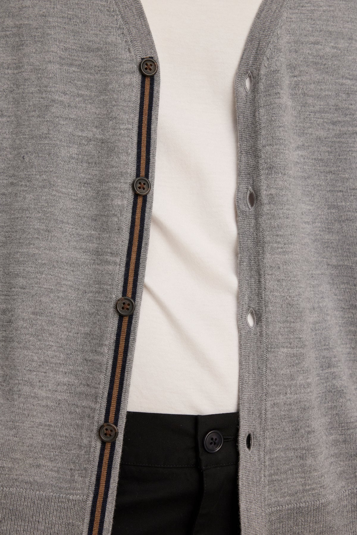 Close-up of a person wearing the unbuttoned SILVIO CARDIGAN by Velvet by Graham & Spencer—a versatile gray V-neck with brown buttons—layered over a white shirt and black pants.-39841095778497