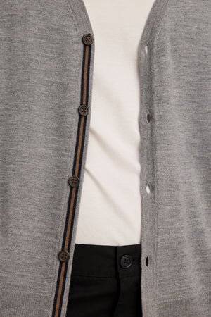Close-up of a person wearing the unbuttoned SILVIO CARDIGAN by Velvet by Graham & Spencer—a versatile gray V-neck with brown buttons—layered over a white shirt and black pants.