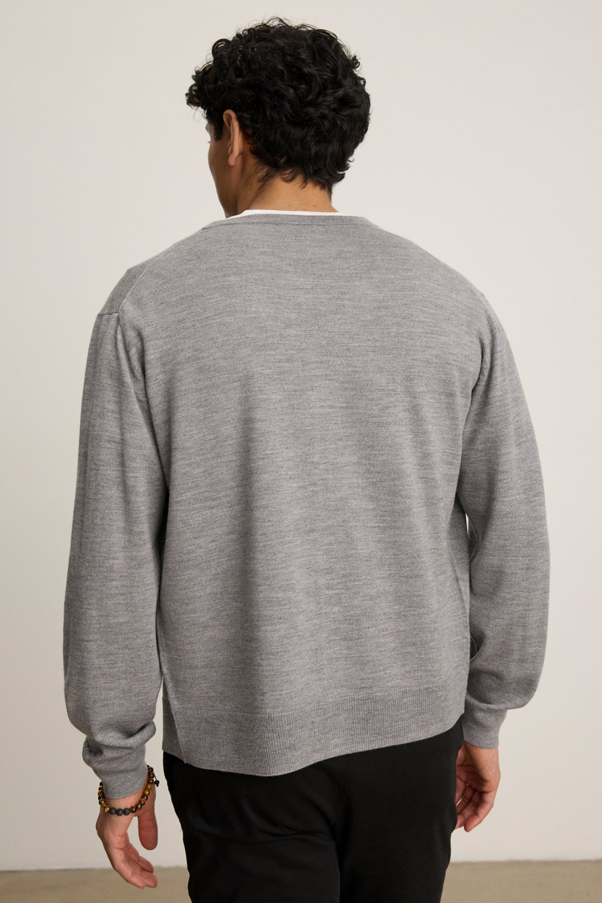 A person stands with their back to the camera, wearing the SILVIO CARDIGAN by Velvet by Graham & Spencer in light gray with black pants against a plain background.-39841095811265