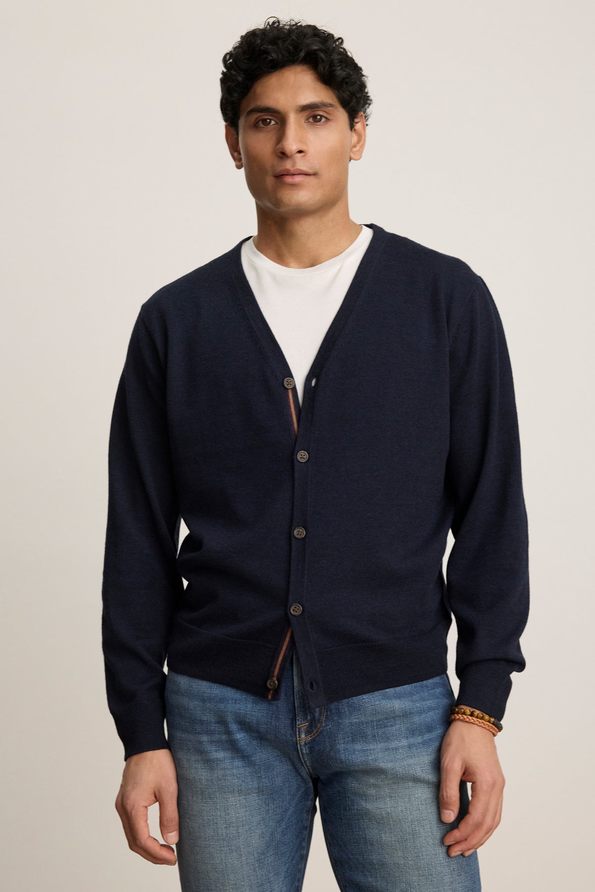 A person wears the SILVIO CARDIGAN by Velvet by Graham & Spencer—a navy blue premium wool cardigan with ribbed trims—over a white T-shirt and blue jeans, standing against a plain light background.-39543530684609