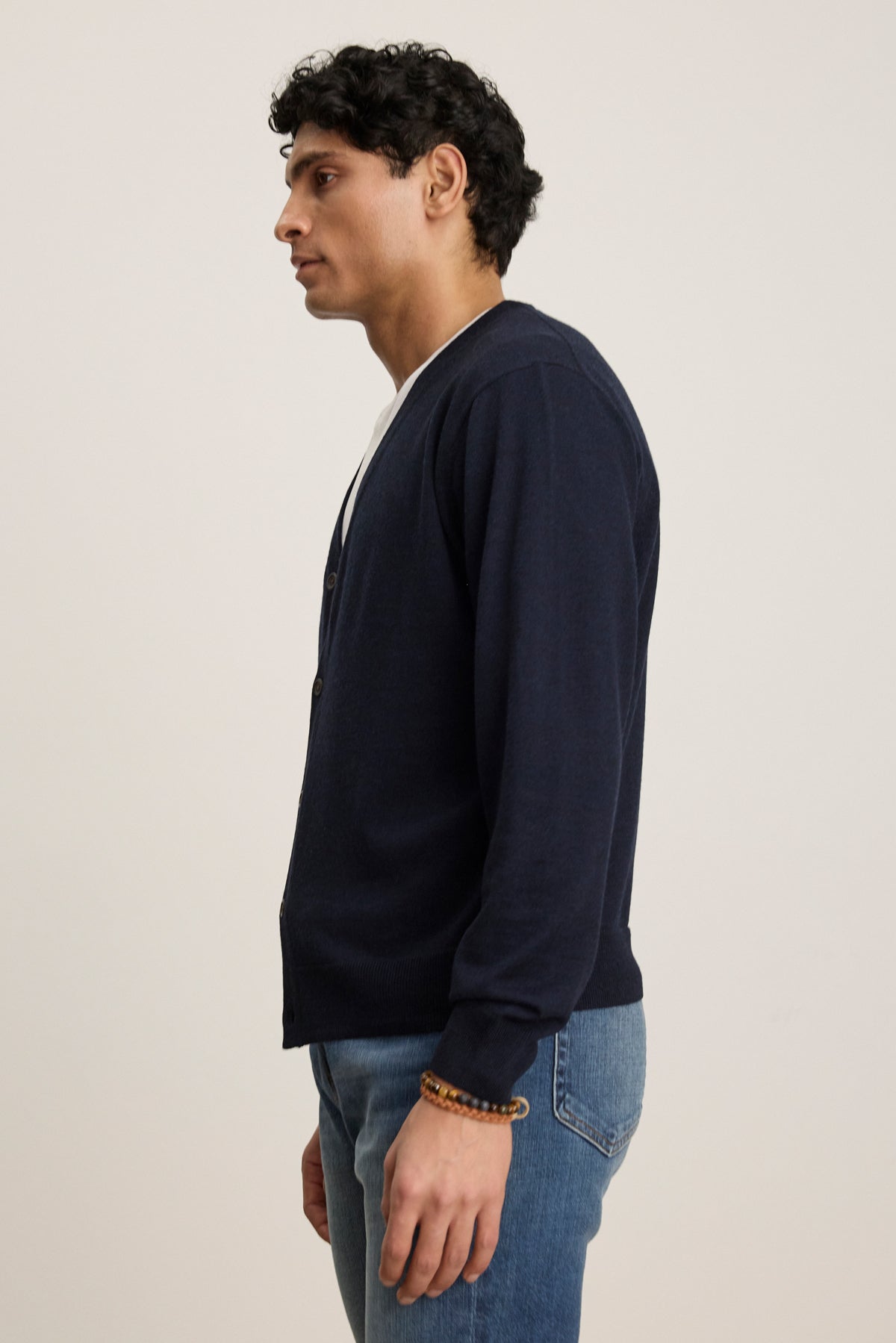 A man stands in profile against a plain background, wearing the Velvet by Graham & Spencer SILVIO CARDIGAN in navy with ribbed trims over a white shirt and blue jeans.-39543530651841