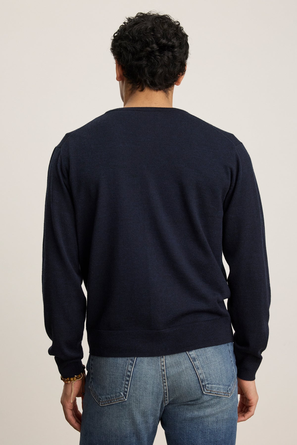 A person is shown from the back against a plain light background, wearing the SILVIO CARDIGAN by Velvet by Graham & Spencer—a dark navy V-neck cardigan with ribbed trims—paired with blue jeans.-39543530619073