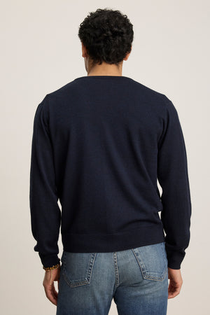 A person is shown from the back against a plain light background, wearing the SILVIO CARDIGAN by Velvet by Graham & Spencer—a dark navy V-neck cardigan with ribbed trims—paired with blue jeans.