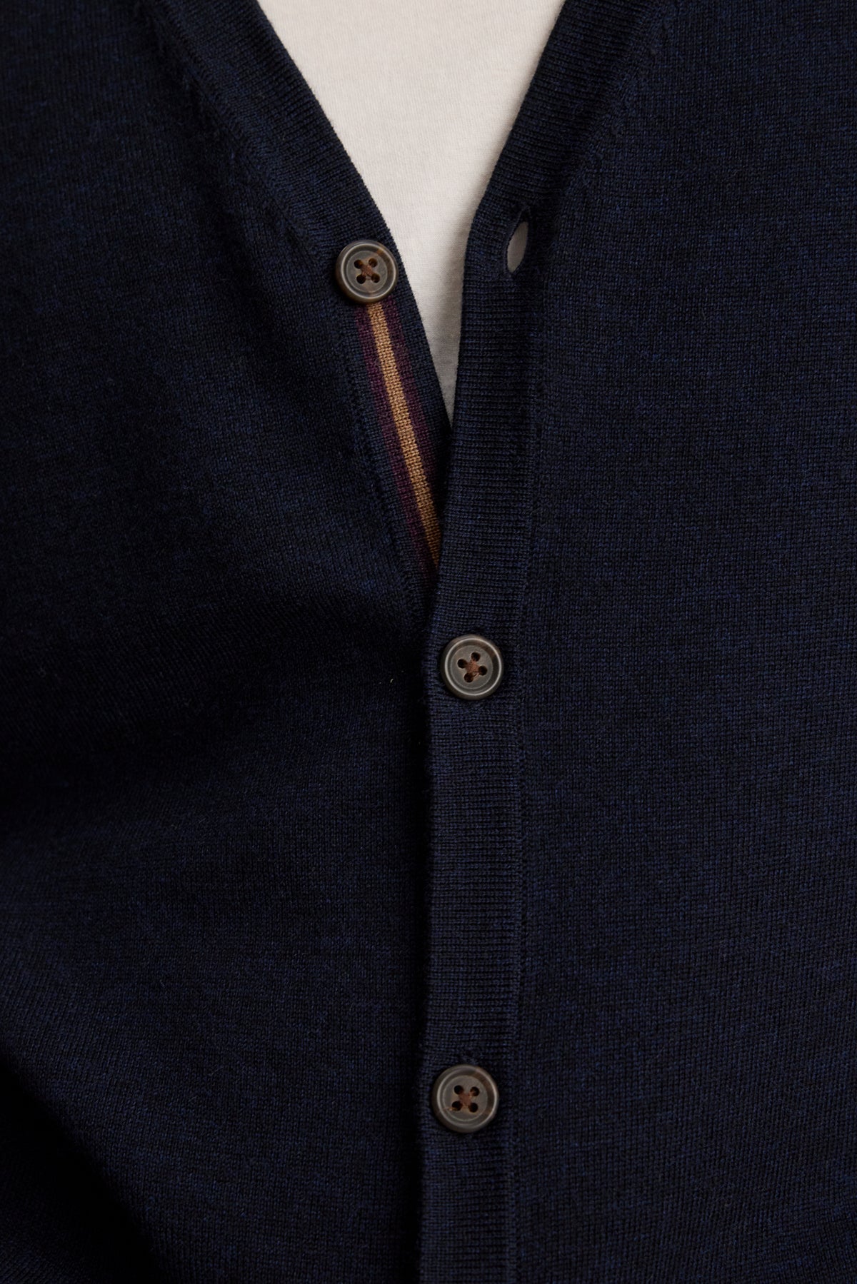 Close-up of the SILVIO CARDIGAN by Velvet by Graham & Spencer: a navy blue wool V-neck with ribbed trims, three brown buttons fastened, and a hint of a white shirt underneath.-39543530553537
