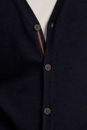 Close-up of the SILVIO CARDIGAN by Velvet by Graham & Spencer: a navy blue wool V-neck with ribbed trims, three brown buttons fastened, and a hint of a white shirt underneath.