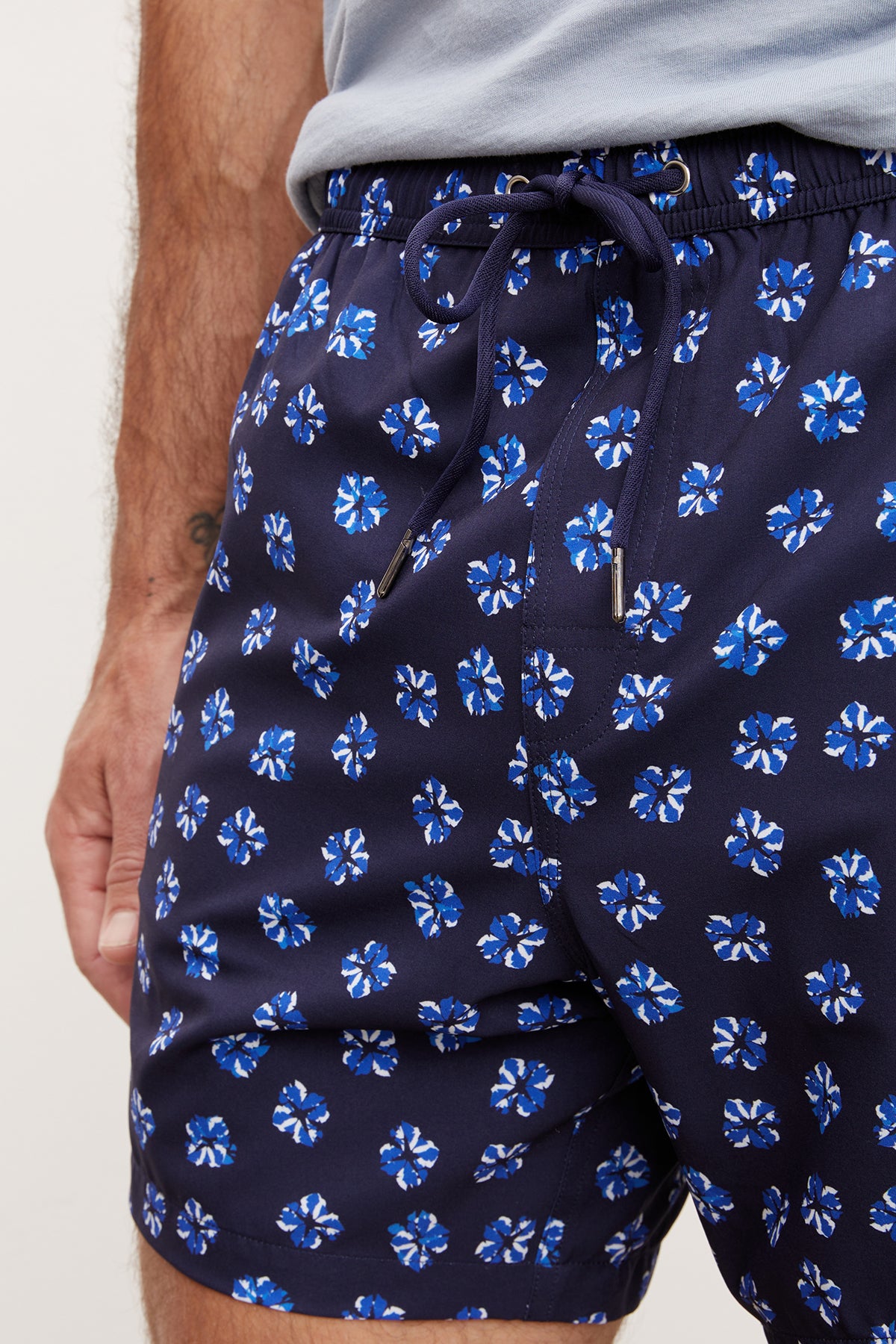 Close-up of a man wearing blue Velvet by Graham & Spencer swim shorts with a vibrant floral print, focusing on the tied drawstring detail.-36918541779137