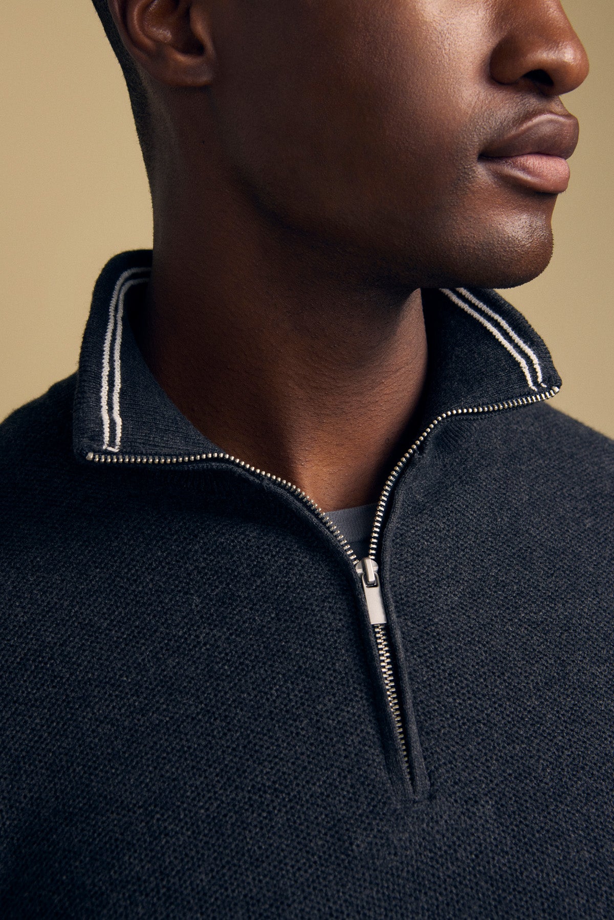 Close-up of a person wearing the BRENTWOOD SWEATER by Velvet by Graham & Spencer, featuring a dark zip-up design with a white-striped collar, showing only the lower half of their face and neck.