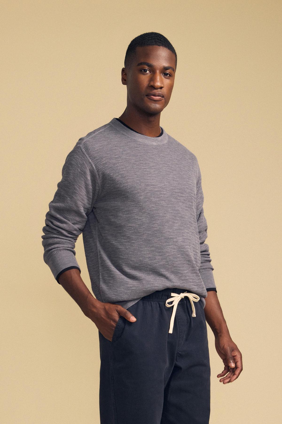 A man wearing a grey CONOR SWEATER and dark drawstring pants.