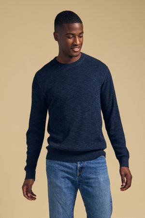 A man wearing a navy blue cotton linen blend CONOR SWEATER by Velvet by Graham & Spencer and blue jeans.