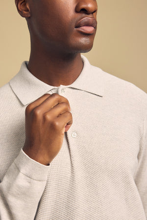 A person wearing the KINGSLEY SWEATER POLO by Velvet by Graham & Spencer in light beige textured cotton-cashmere holds the collar, shown from the shoulders up against a neutral background.