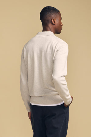 A person stands facing away from the camera wearing the light beige KINGSLEY SWEATER POLO by Velvet by Graham & Spencer and dark pants against a plain beige background.