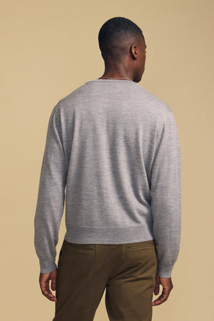 A man stands with his back to the camera, wearing the Velvet by Graham & Spencer SILVIO CARDIGAN in light gray and olive green pants, set against a beige background.