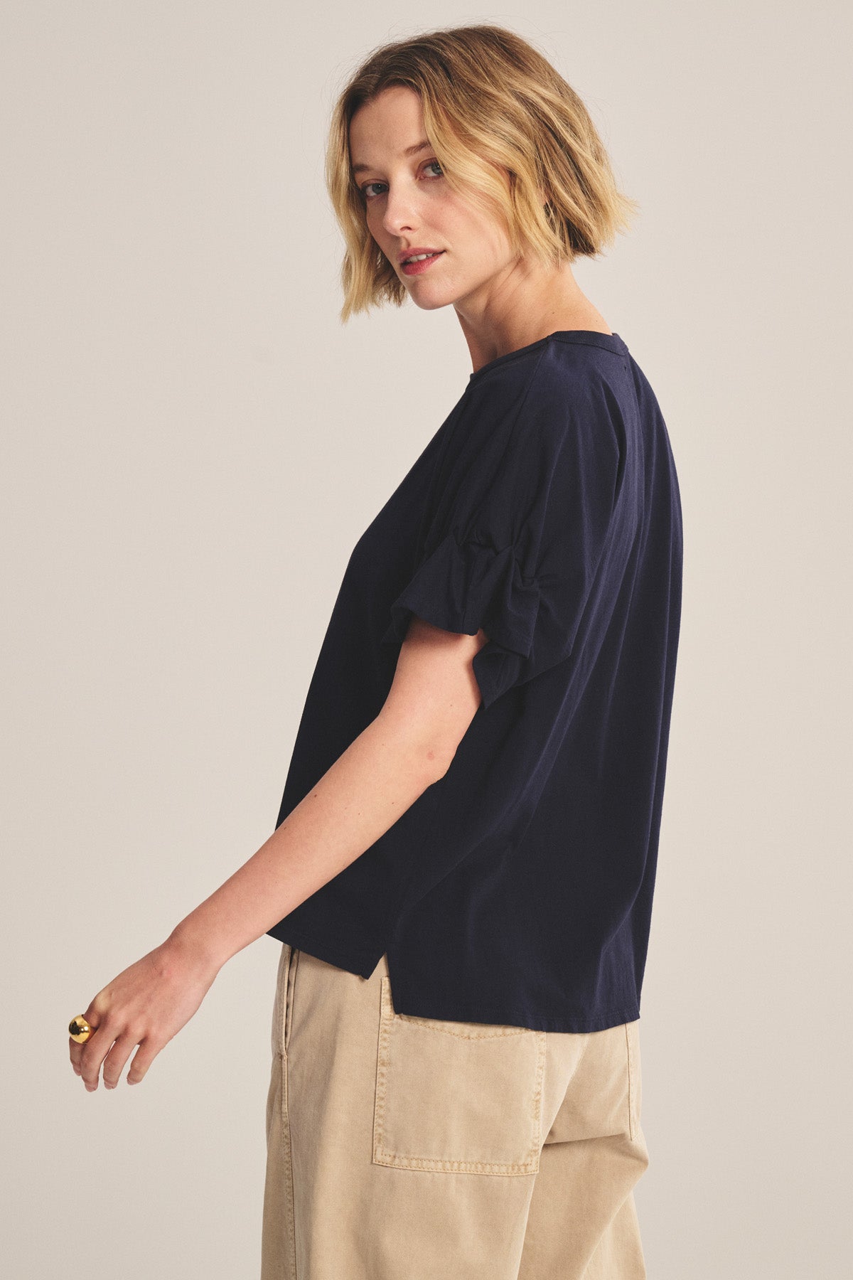 A woman with short blonde hair wears the Velvet by Graham & Spencer TAE TEE, a navy relaxed-fit cotton jersey top with puffed sleeves, and beige pants, standing sideways against a neutral background.-41008416751809