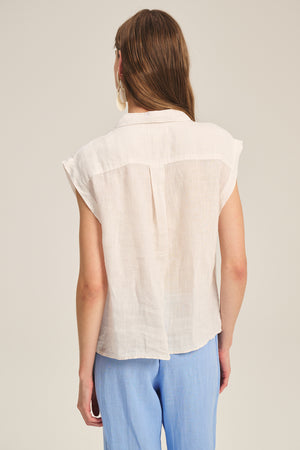 A person with long brown hair is shown from the back wearing the Velvet by Graham & Spencer TASHA LINEN TOP, a sleeveless lightweight style, paired with light blue pants against a plain background.