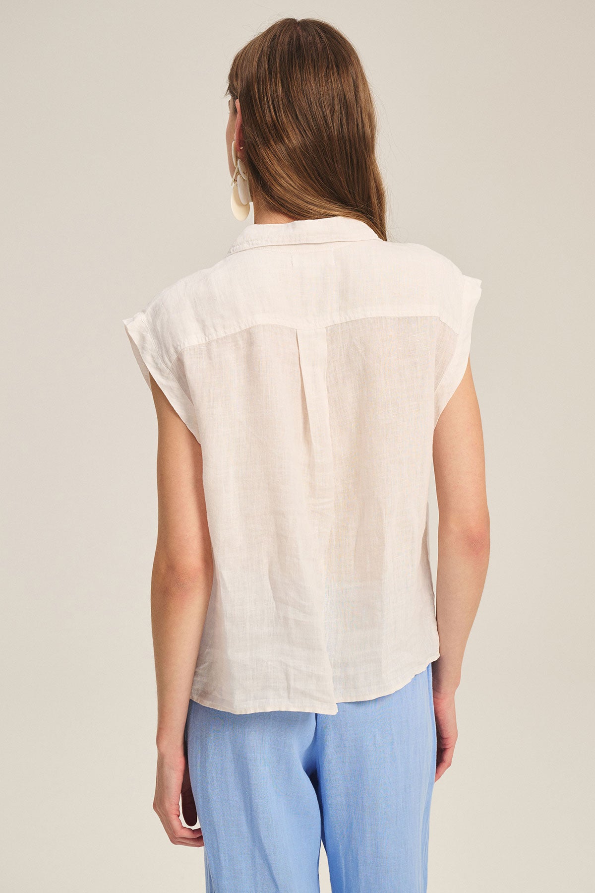 A person with long brown hair is seen from the back wearing the TASHA LINEN TOP by Velvet by Graham & Spencer and light blue pants against a plain background.-39725079756993