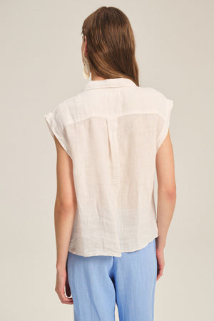 A person with long brown hair is seen from the back wearing the TASHA LINEN TOP by Velvet by Graham & Spencer and light blue pants against a plain background.