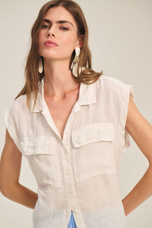 A woman wears the TASHA LINEN TOP by Velvet by Graham & Spencer, a sleeveless lightweight cargo top with front pockets, paired with large white drop earrings against a neutral background.