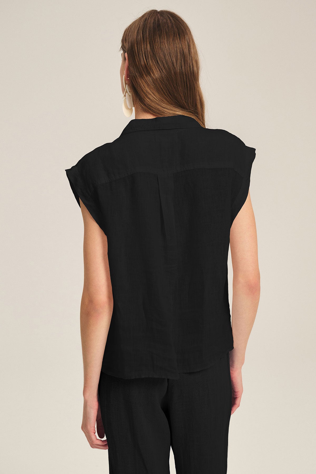 A person with long brown hair is shown from the back, wearing the Velvet by Graham & Spencer TASHA LINEN TOP in black with matching black pants, set against a plain light background.-39725079658689