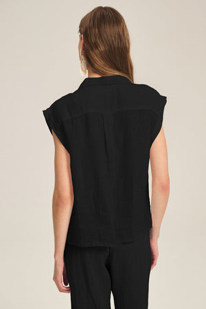 A person with long brown hair is shown from the back, wearing the Velvet by Graham & Spencer TASHA LINEN TOP in black with matching black pants, set against a plain light background.