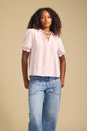 A woman with curly hair wears the TATUM TEE by Velvet by Graham & Spencer, paired with light blue jeans, standing against a beige background.