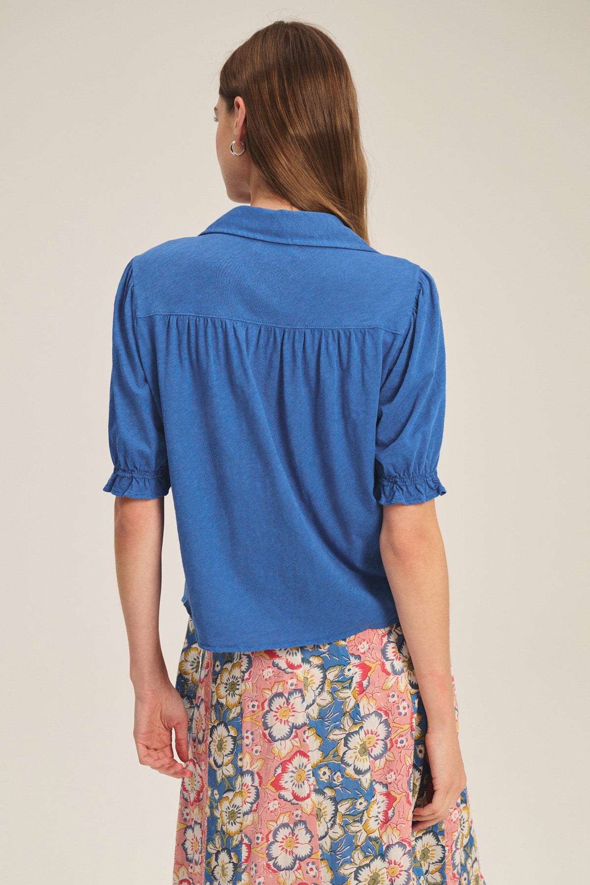 A woman with long brown hair is seen from behind, wearing the TATUM TEE by Velvet by Graham & Spencer and a pink floral skirt.-41178014646465