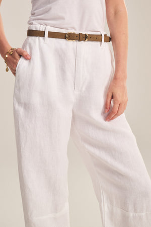 Person wearing a white shirt and Velvet by Graham & Spencer TAYLOR HEAVY LINEN PANT with a brown belt, left hand in pocket, and gold bracelet on right wrist.